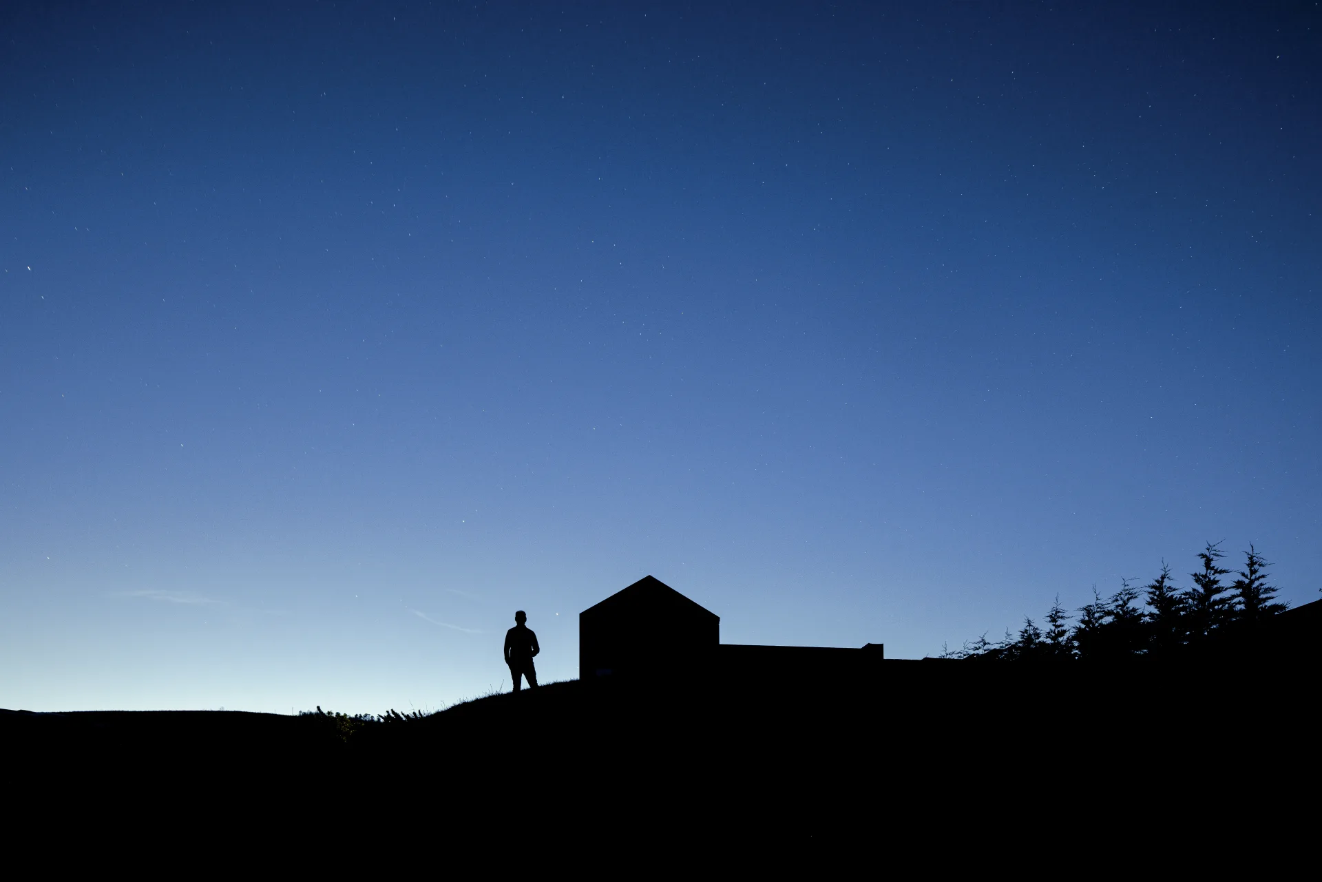 Silhueta de uma pessoa e de uma casa sob o céu azul ao anoitecer